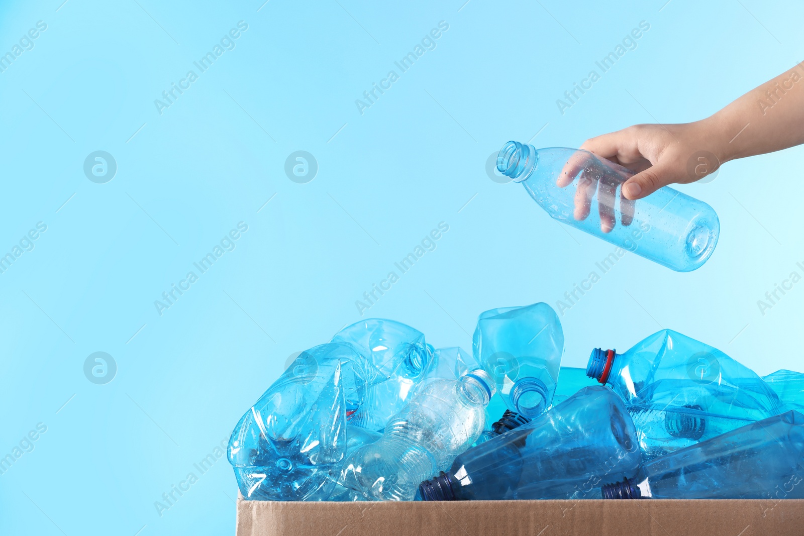 Photo of Woman putting used plastic bottle into cardboard box on color background, closeup with space for text. Recycling problem