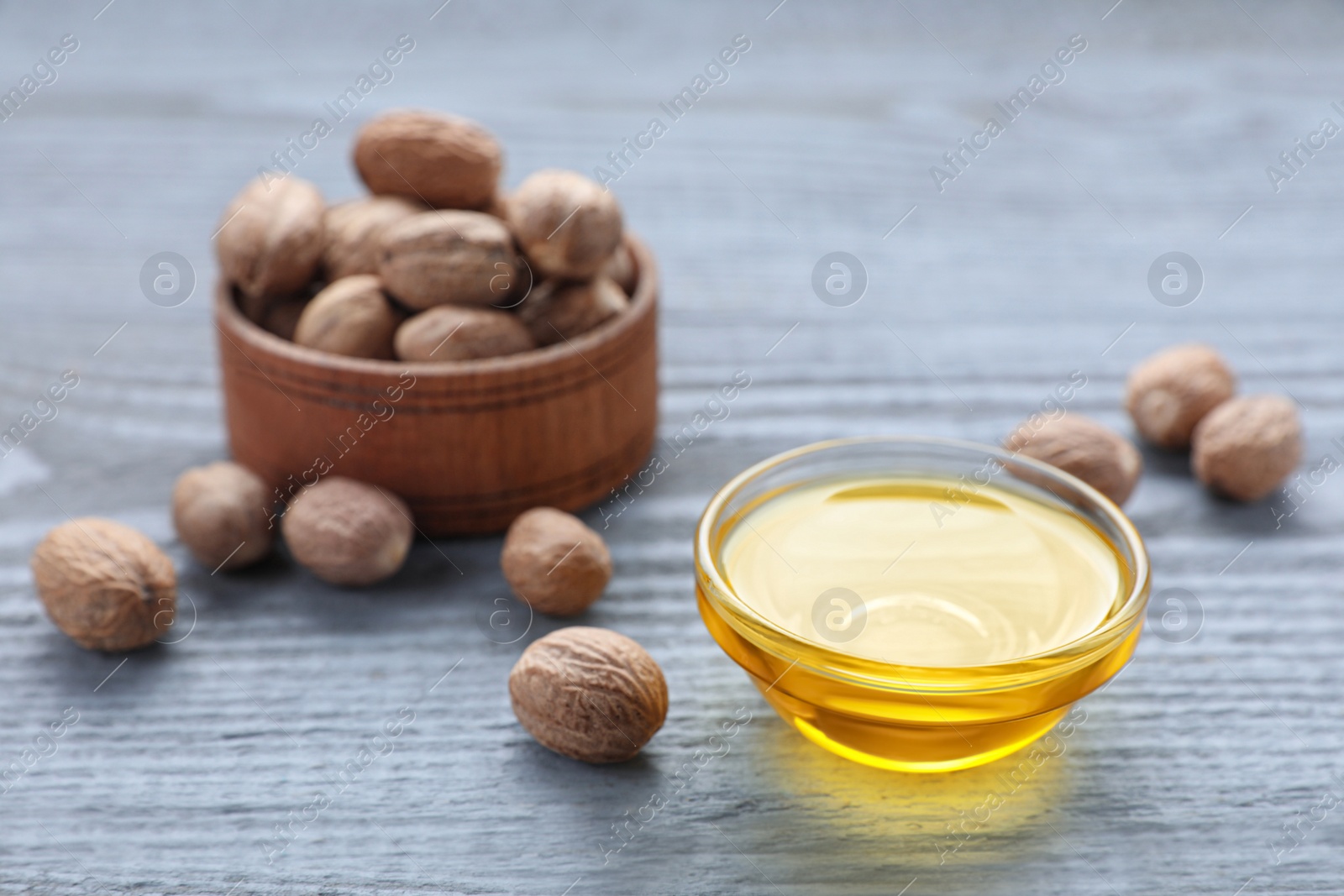 Photo of Bowl of nutmeg oil and nuts on grey wooden table, closeup