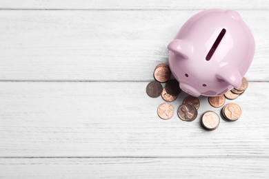 Photo of Top view of piggy bank and cents on white wooden table, space for text. Money savings