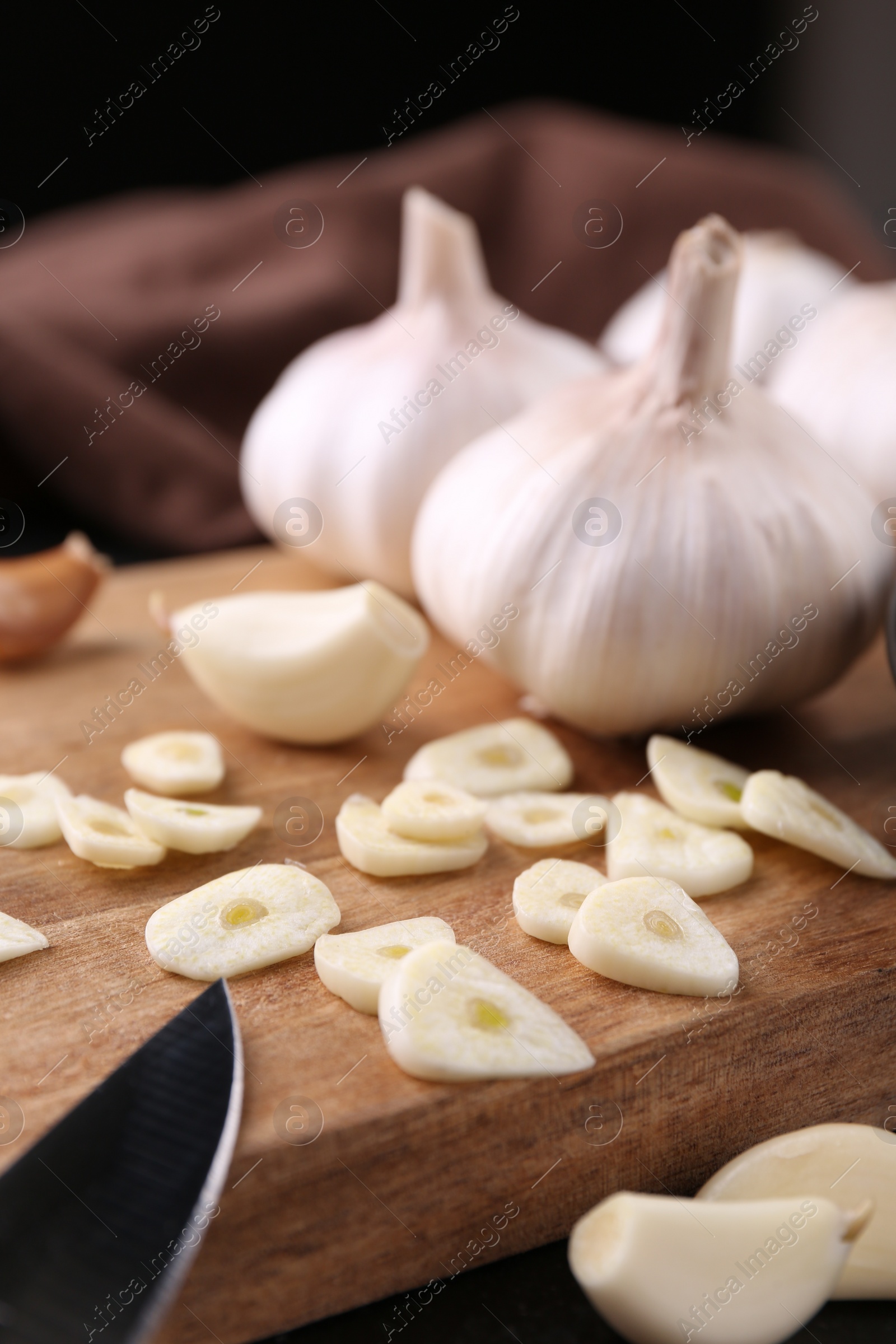 Photo of Aromatic cut garlic, cloves and bulbs on dark table, closeup