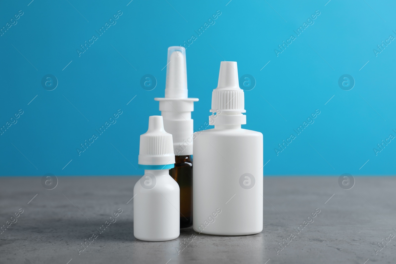 Photo of Nasal sprays in different bottles on grey table against light blue background