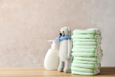 Photo of Stack of diapers, toy bear and cream on table against color background, space for text. Baby accessories