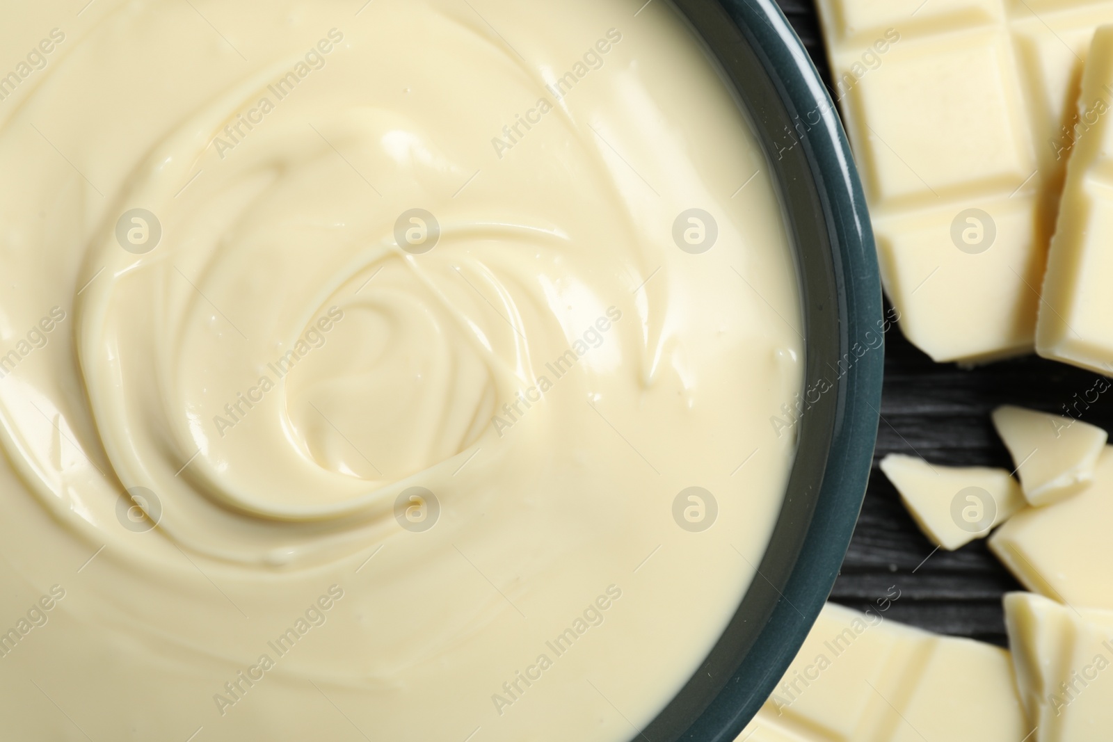 Photo of Tasty white chocolate paste in bowl and pieces on table, top view