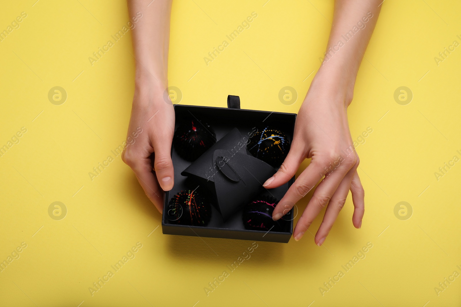 Photo of Woman with box of delicious chocolate candies on yellow background, top view