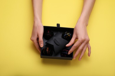 Photo of Woman with box of delicious chocolate candies on yellow background, top view