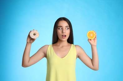 Photo of Woman choosing between orange and doughnut on light blue background