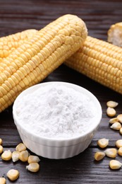 Photo of Bowl with corn starch, ripe cobs and kernels on dark wooden table