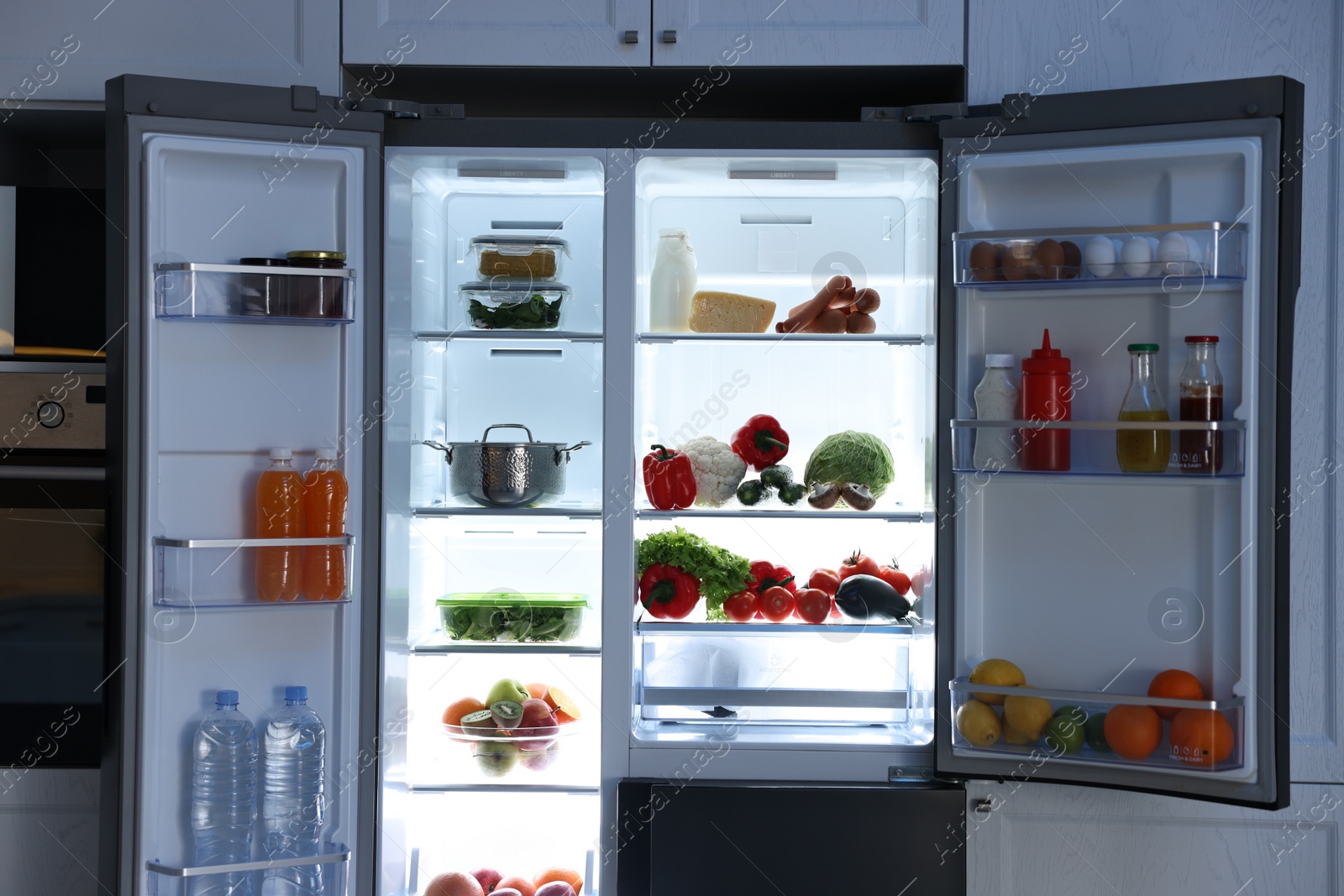 Photo of Open refrigerator full of different products in kitchen