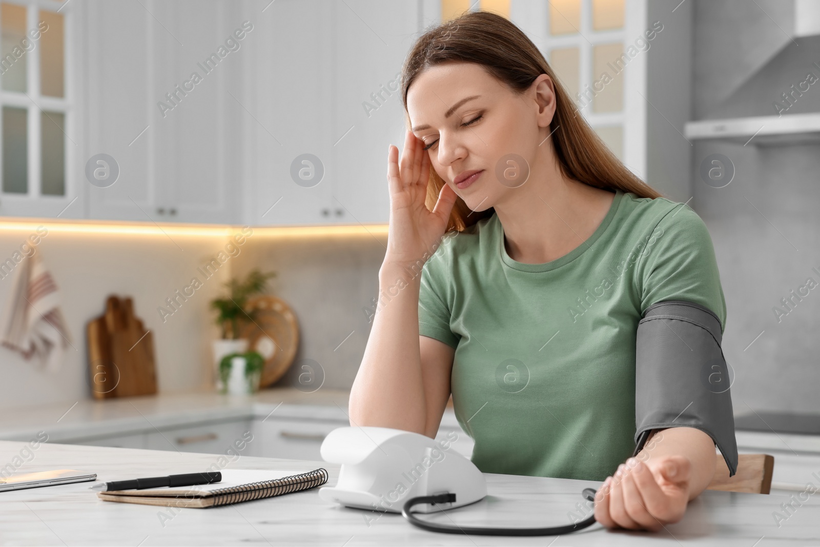 Photo of Woman suffering from headache and measuring blood pressure in kitchen, space for text