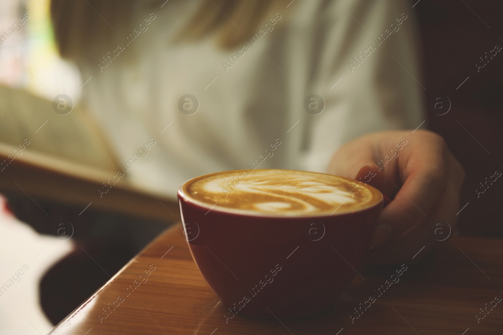 Image of Woman with coffee reading book indoors, focus on cup