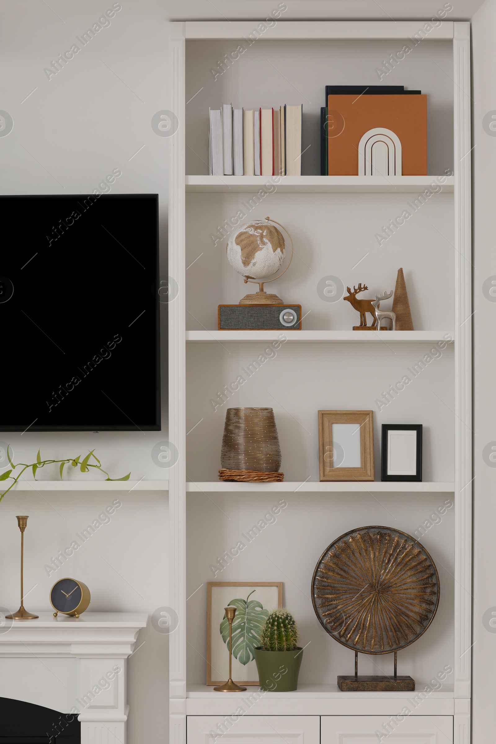 Photo of Stylish shelves with different decor elements and TV set in room. Interior design