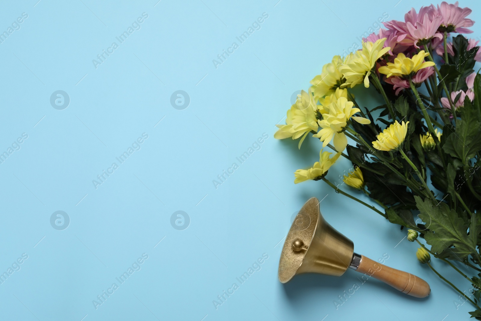 Photo of Golden school bell and bouquet of beautiful chrysanthemum flowers on light blue background, flat lay. Space for text