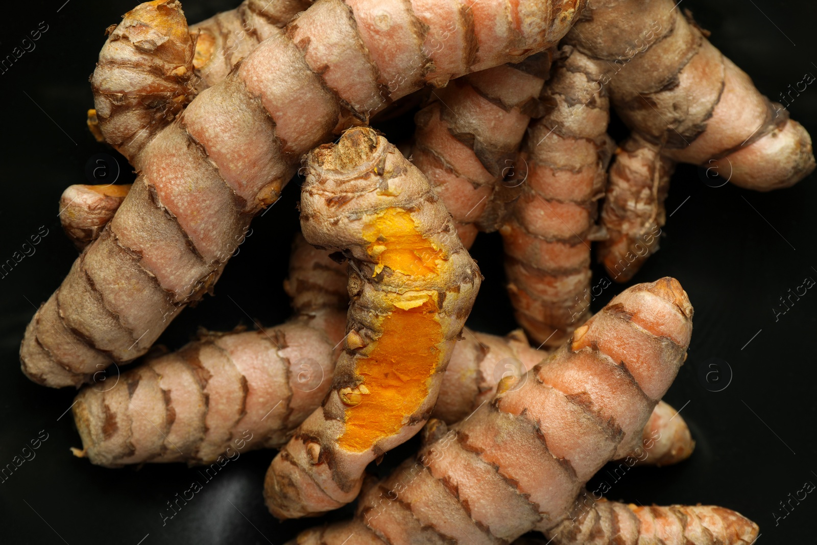Photo of Many raw turmeric roots on black background, closeup