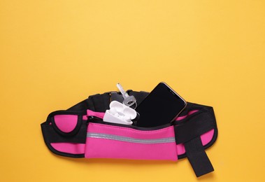 Photo of Stylish pink waist bag with smartphone, key and earphones on orange background, flat lay. Space for text