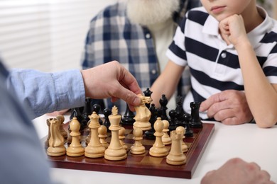 Family playing chess together at table indoors, closeup