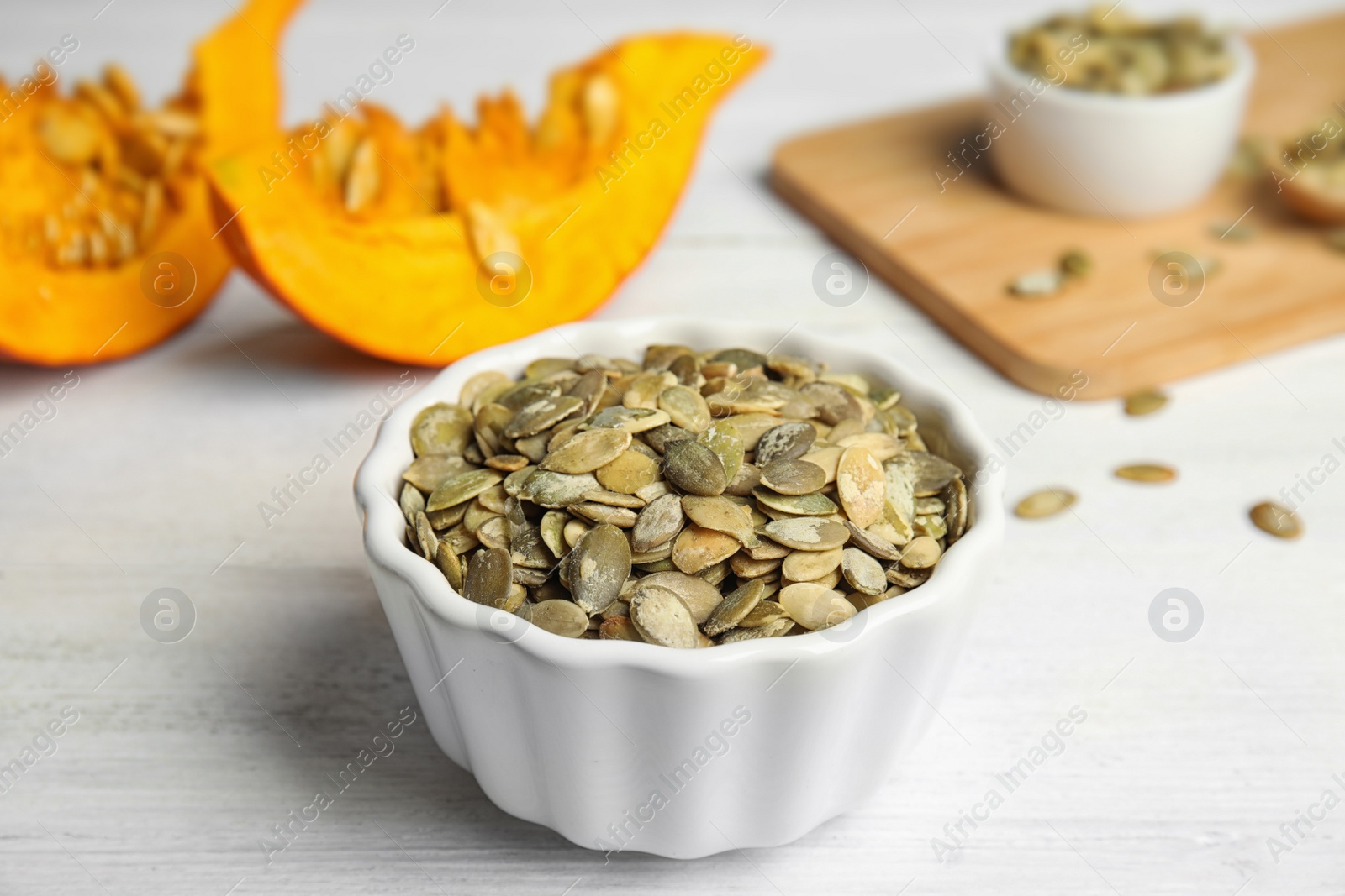 Photo of Bowl of raw pumpkin seeds on white wooden table