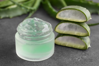 Photo of Jar of natural gel and sliced aloe vera leaves on grey table, closeup