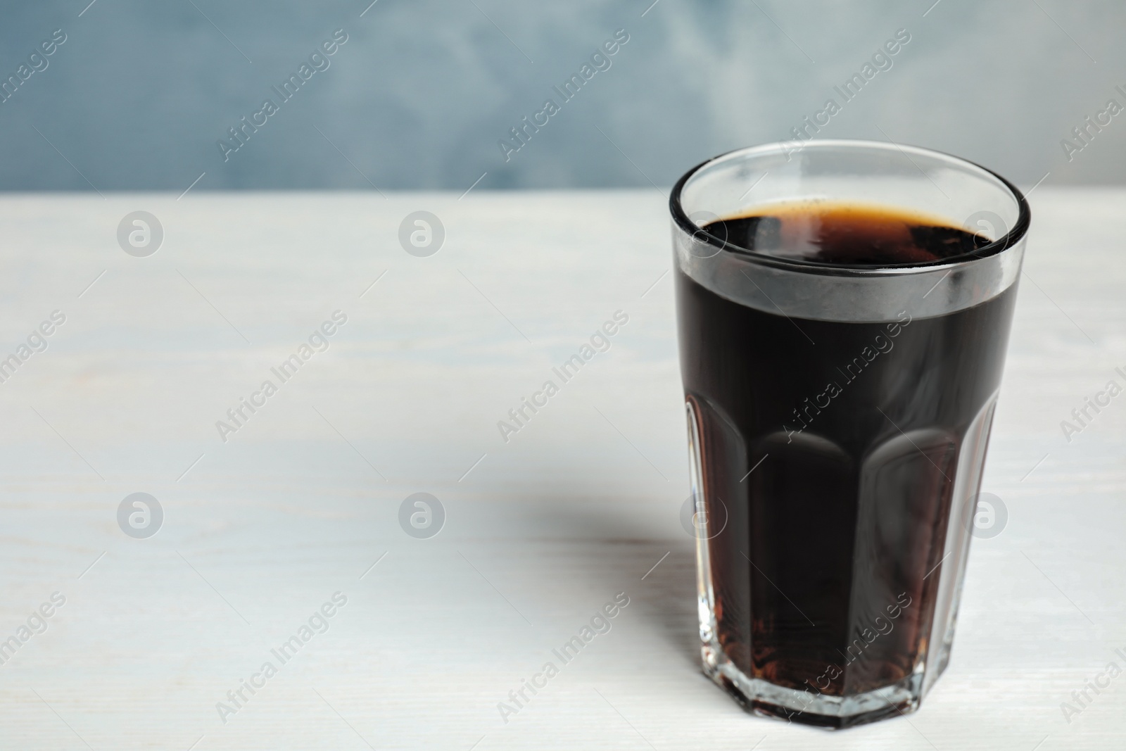 Photo of Glass of refreshing soda drink on white wooden table against blue background. Space for text
