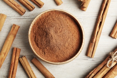 Aromatic cinnamon powder and sticks on white wooden table, flat lay
