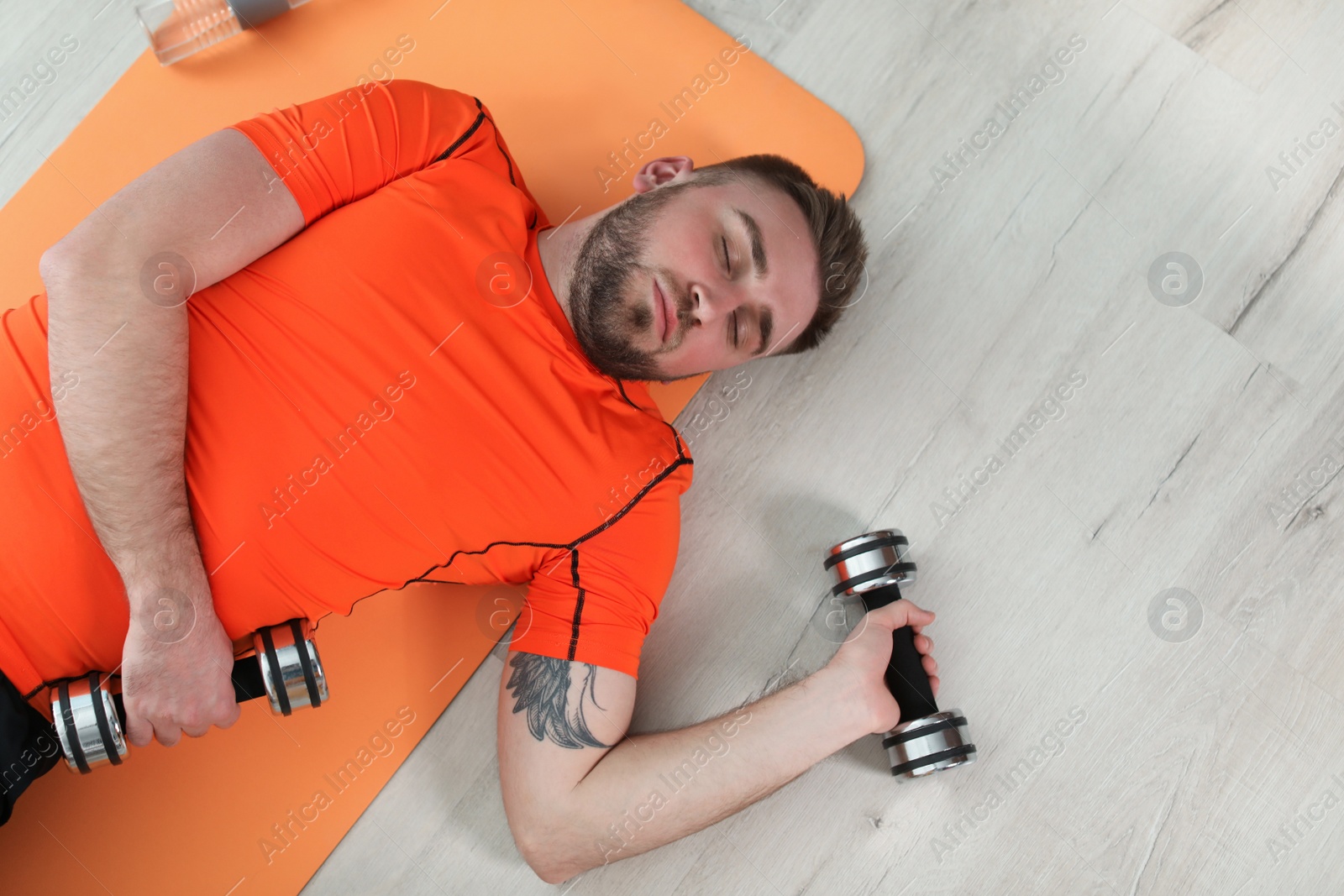 Photo of Lazy young man with sport equipment on floor at home, top view