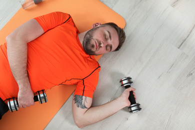 Photo of Lazy young man with sport equipment on floor at home, top view