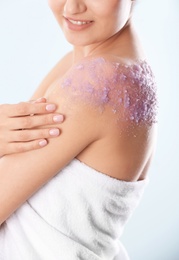 Young woman with natural scrub on her body against light background