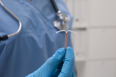 Photo of Doctor holding T-shaped intrauterine birth control device on blurred background, closeup