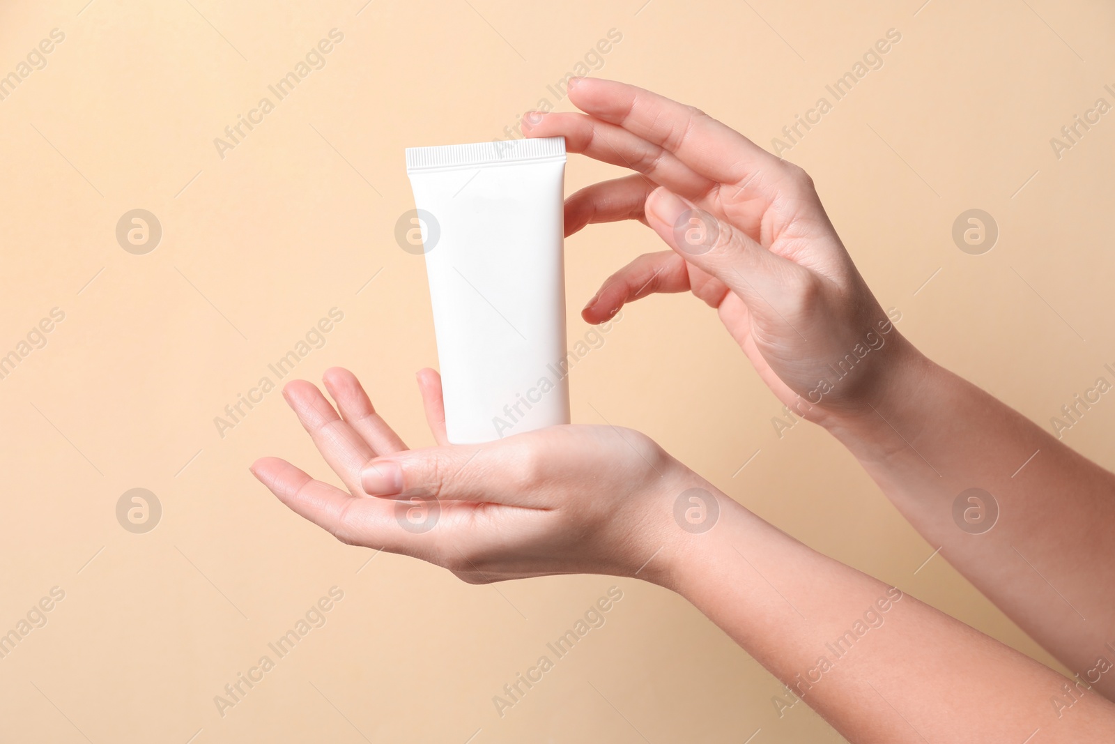 Photo of Woman with tube of hand cream on beige background, closeup