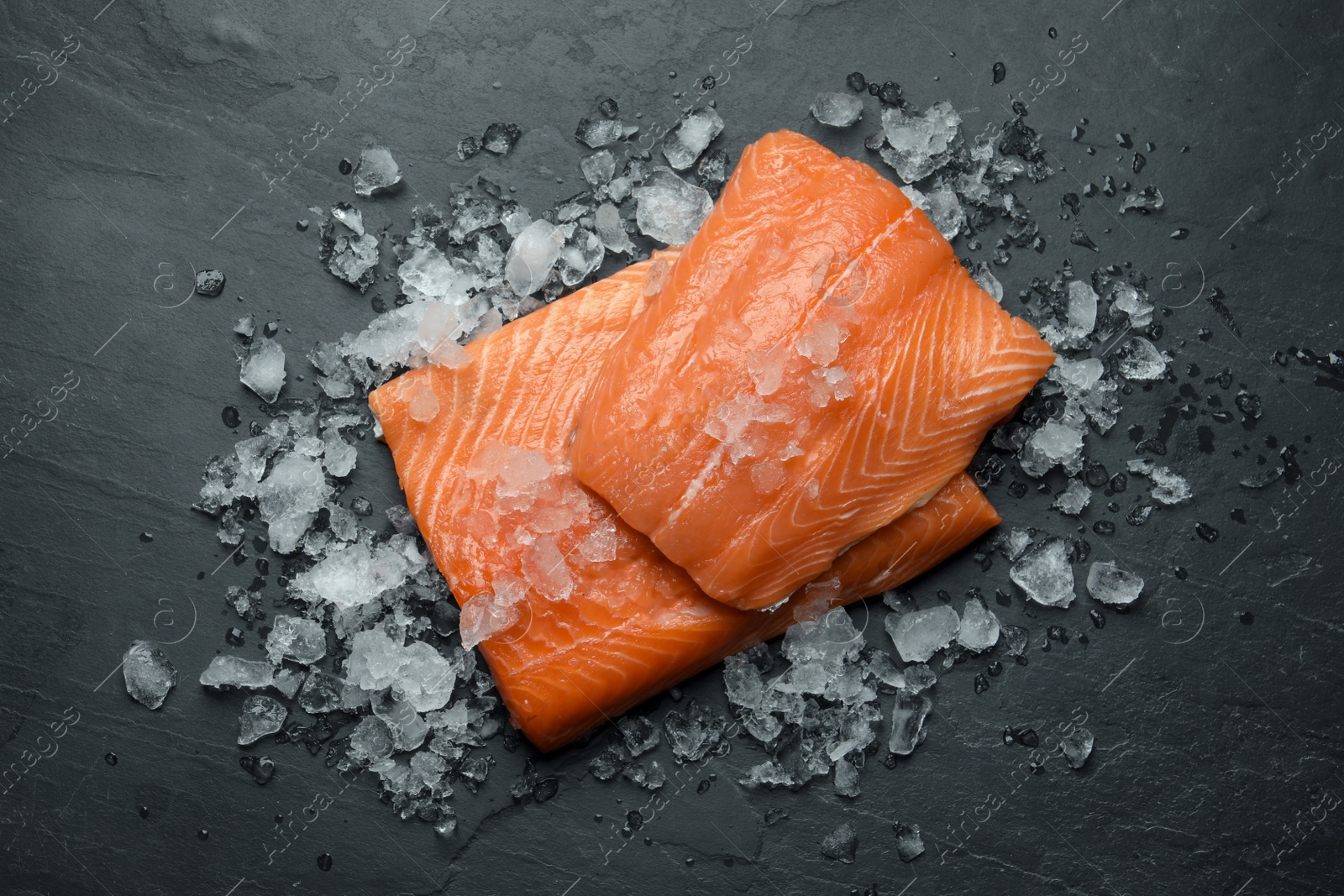 Photo of Fresh raw salmon with ice on black table, flat lay