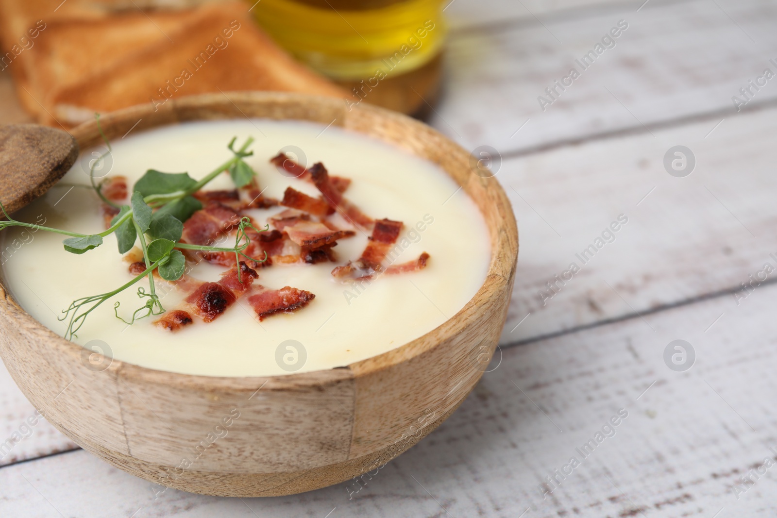 Photo of Delicious potato soup with bacon and microgreens in bowl on wooden table, closeup. Space for text