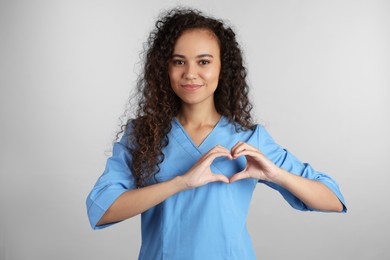 Photo of Happy young African-American doctor making heart with hands on light grey background