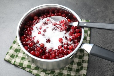Making cranberry sauce. Fresh cranberries with sugar in saucepan and spoon on gray table, closeup