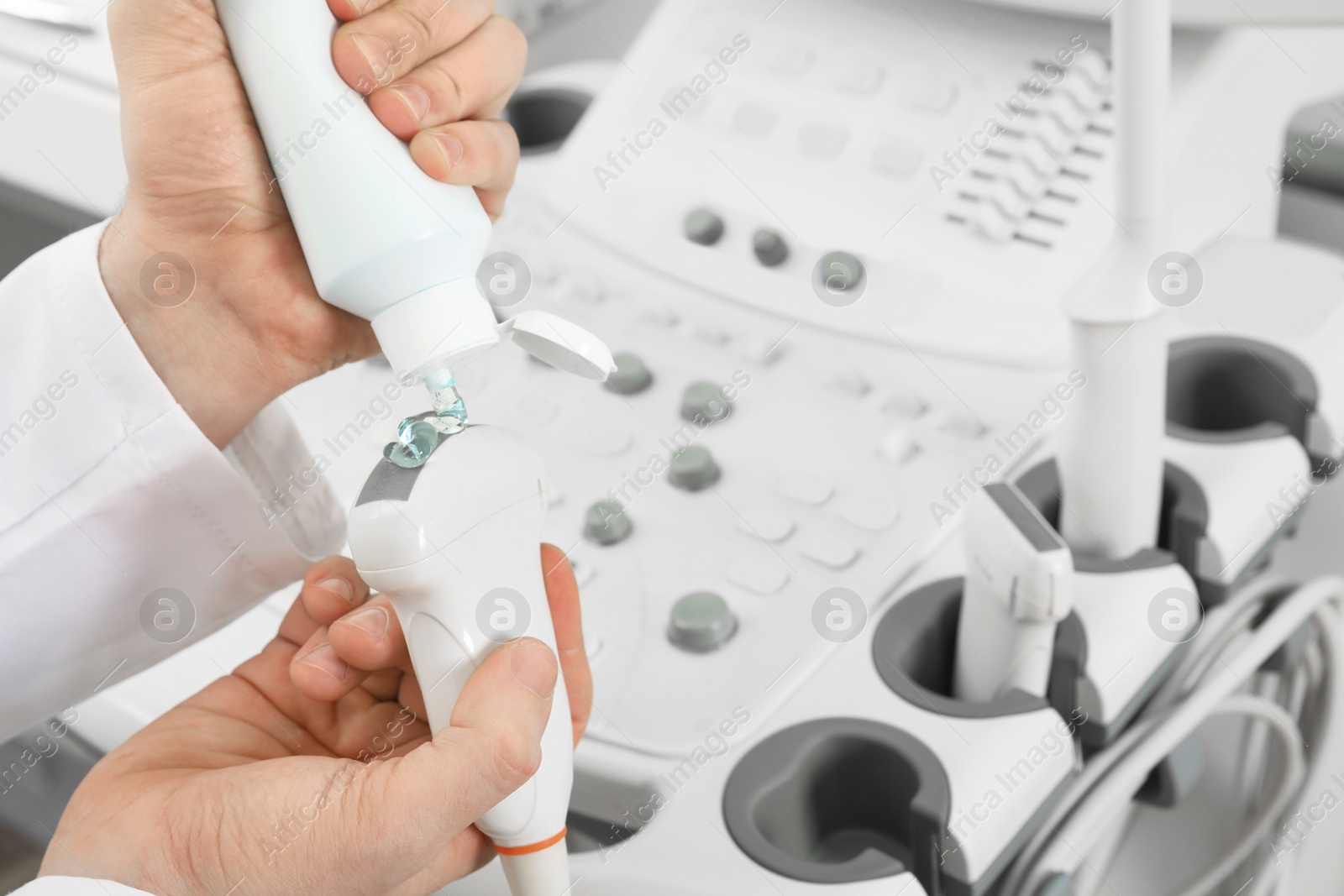 Photo of Sonographer covering ultrasound machine probe with gel in clinic, closeup