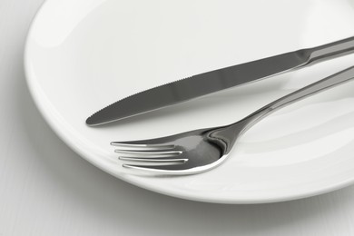 Photo of Clean plate, fork and knife on white table, closeup