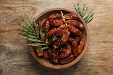 Bowl of sweet dried dates on wooden table, top view