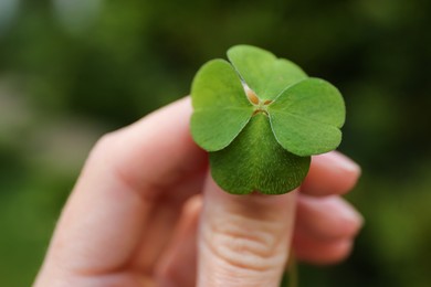 Photo of Woman holding beautiful green four leaf clover outdoors, closeup