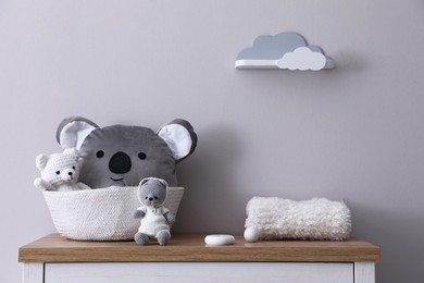 Photo of Child's toys, wicker basket and plaid on chest of drawers near light grey wall indoors