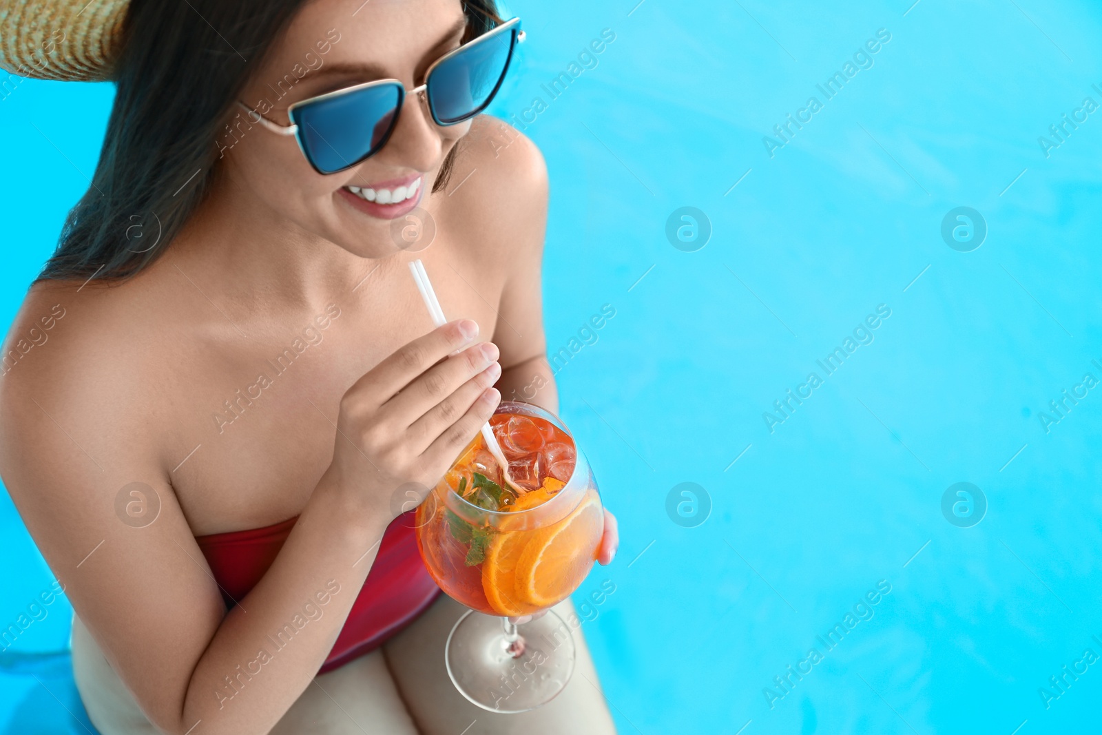 Photo of Woman with glass of refreshing drink in swimming pool, closeup