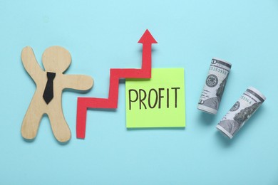 Photo of Sticky note with word Profit, rolled banknotes, up arrow and wooden human figure on turquoise background, flat lay