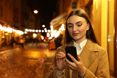 Photo of Beautiful woman using smartphone on night city street. Space for text