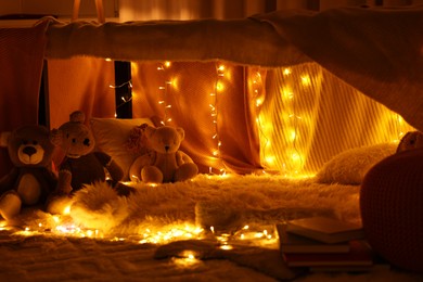 Photo of Beautiful play tent decorated with festive lights and toys at home