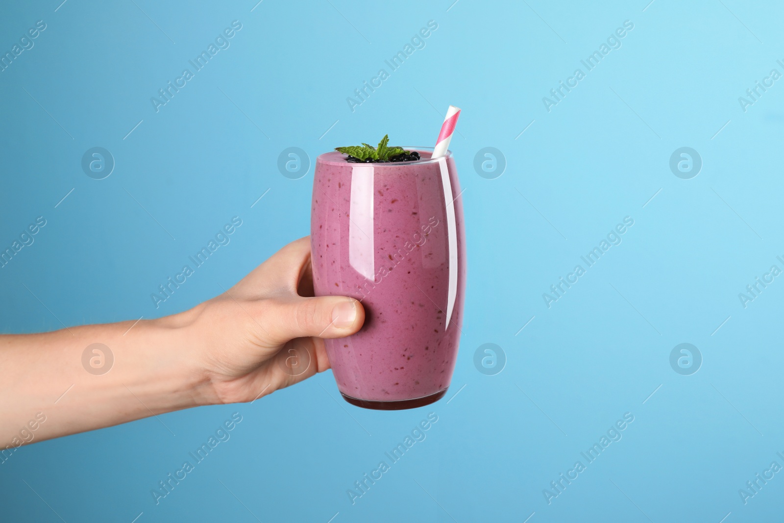 Photo of Young woman holding glass of tasty blackberry smoothie on light blue background, closeup