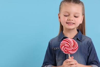 Photo of Happy little girl with bright lollipop swirl on light blue background, space for text