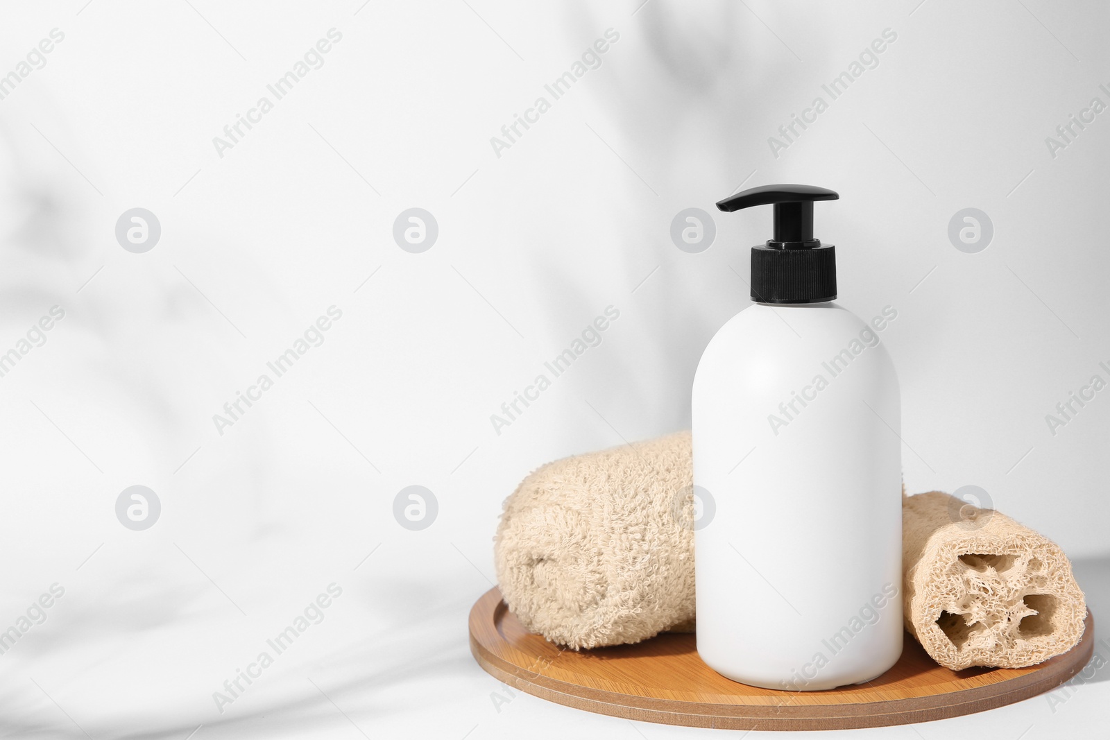 Photo of Bottle with cosmetic product, rolled towel and loofah sponge on white background. Space for text