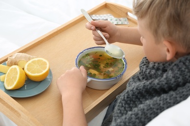 Photo of Sick little boy eating broth to cure cold in bed at home