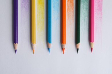 Colorful pencils with swatches on white background, top view