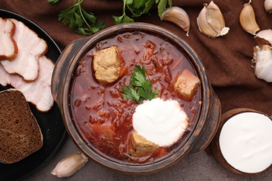 Photo of Tasty borscht with sour cream in bowl served on brown textured table, flat lay
