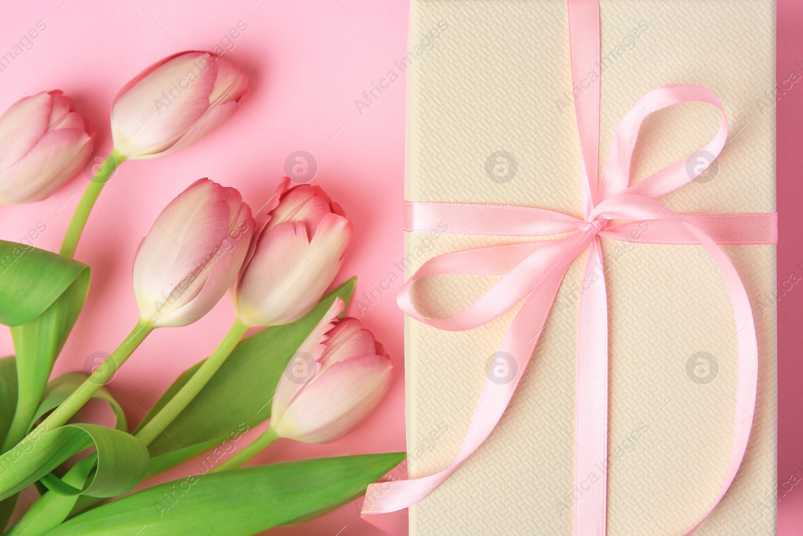 Photo of Beautiful gift box with bow and tulips on pink background, flat lay