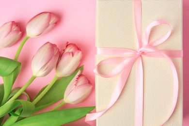 Photo of Beautiful gift box with bow and tulips on pink background, flat lay