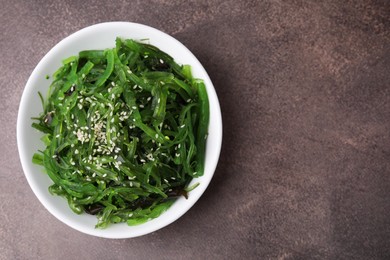 Photo of Tasty seaweed salad in bowl on brown table, top view. Space for text